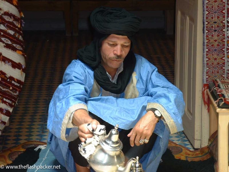 man in blue berber robes pouring tea