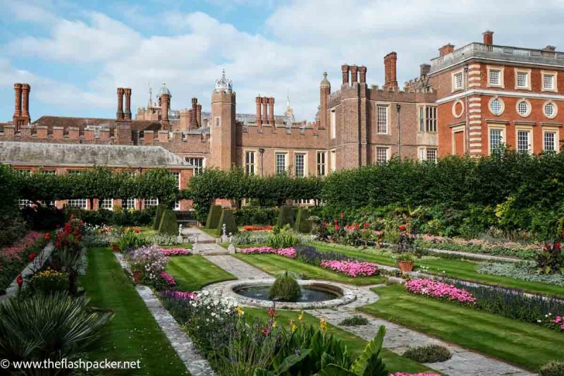 formal garden with pink flowers in front of red brick palace