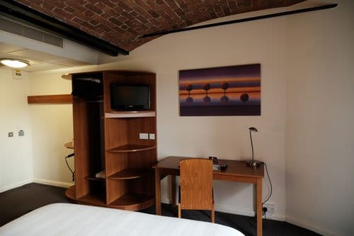 hotel bedroom showing foot of bed with desk and shelves