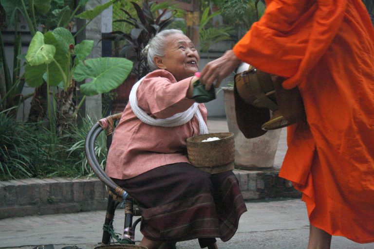 old woman giving alms to monk in saffron robe as an example of authentic travel