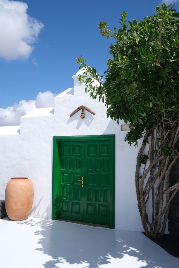 whitewashed building with green door framed by a tree and a large earthenware pot