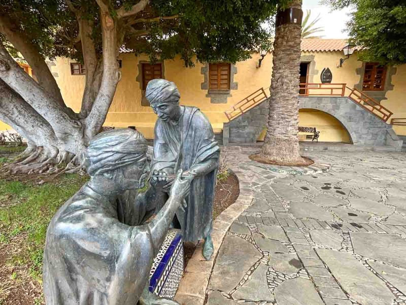 bronze sculpture of two men waering headdresses in front of mustard coloured colonial building