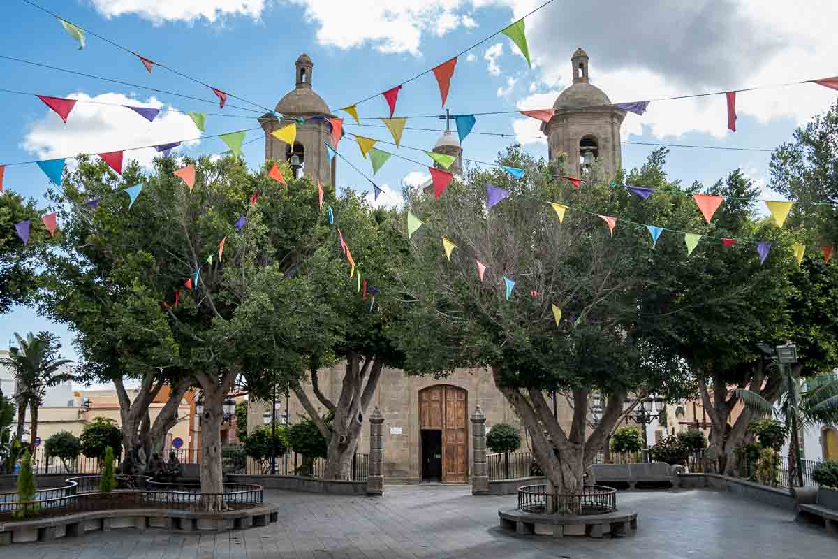 church with 2 bell towers fronted by a town square planted with trees