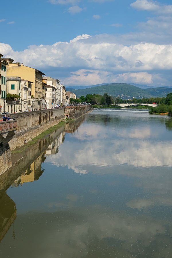 view along the river arno with bridge and mountains in distance