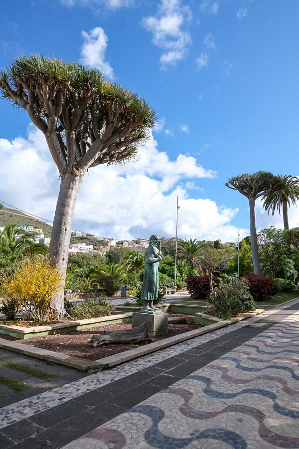 pathway in park lined with tropical tress and a statue of a woman