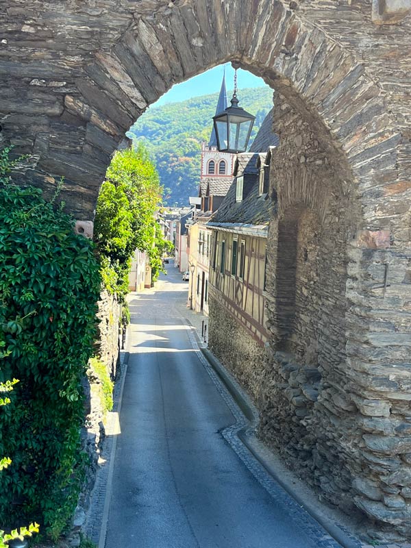 view of medieval buildings of bacharach germany and church spire through a stone arch