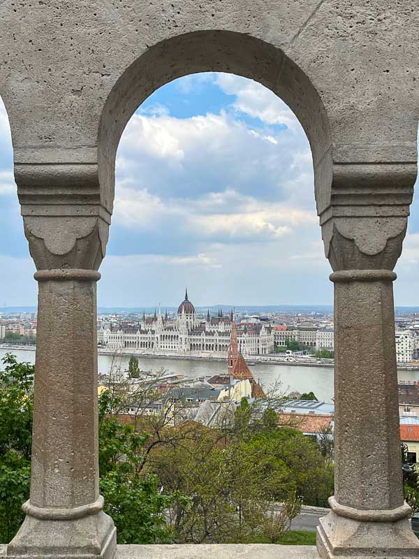 view of the river danube and parliament building in budapest seen through arch of fishermens bastion