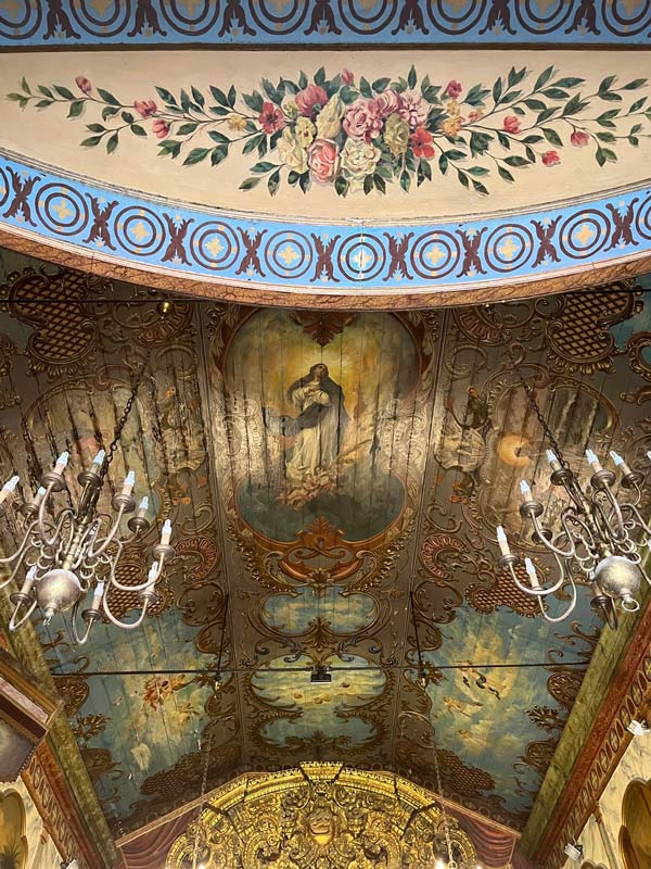 ornate painted ceiling of a small chuch with 2 chandeliers