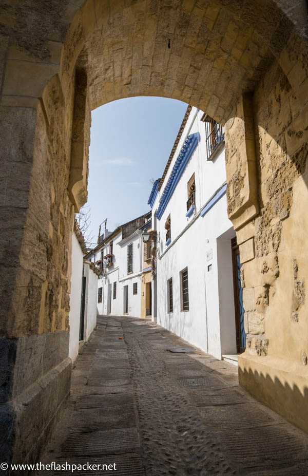 narrow street of whitewashed buildings seen through a stone arch in the old town of cordoba spain