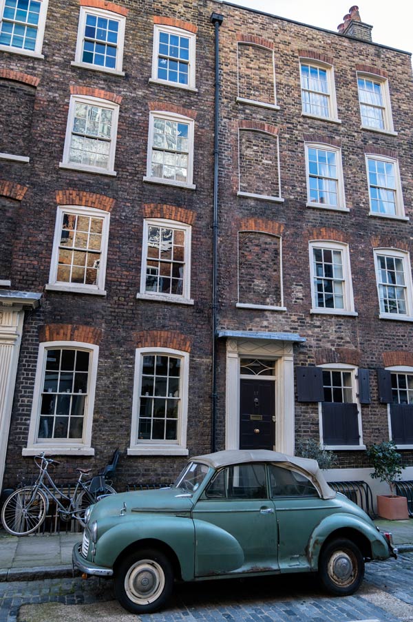 blue vintage car parked in street of tall terraced houses