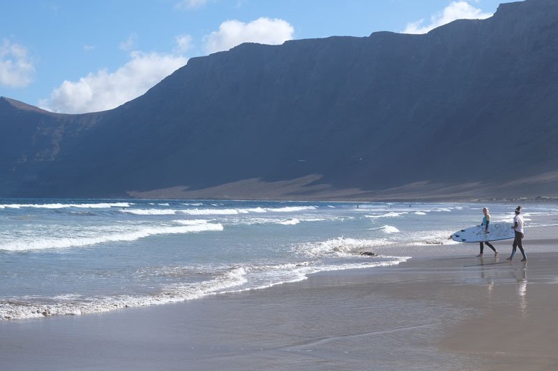 2 people with a surfboard on the beach at famara lanzarote