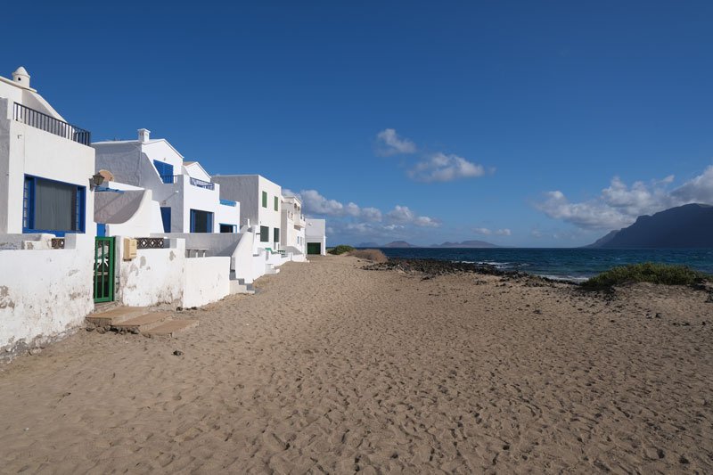 whitewashed bungalows at the edge of a sandy famara lbeach in lanzarote