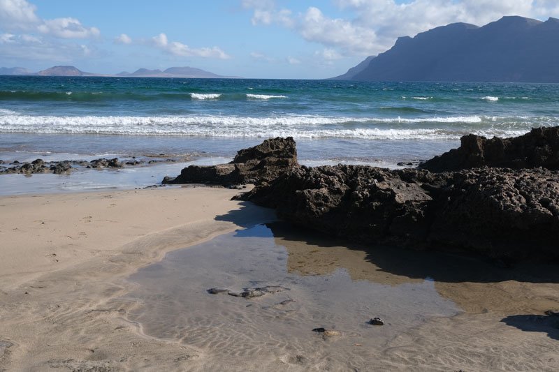 sandy beach with rock pool and cliffs in distance