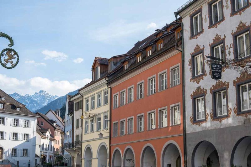 porticoed 2-storey medieval buildings in street in feldkirch with snow capped mountains in distance