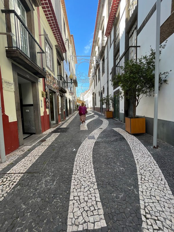 female solo traveller in Madeira walking along a narrow street paved with black and white mosaics 