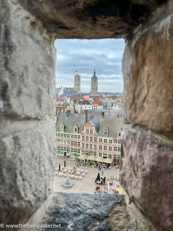 view of a medieval square with tower of church in background through a stone window frame