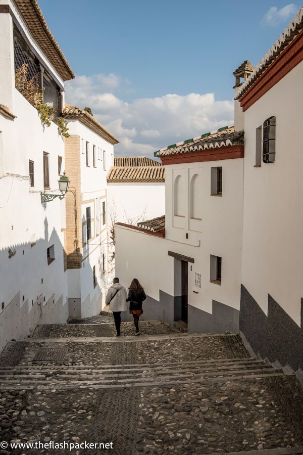 two people walking down a set of stone steps between pretty whitewashed buildings