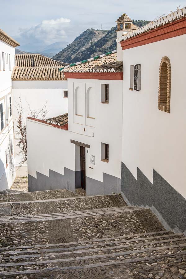 steep steps leading downhill between whitewashed buildings with mountains in distance