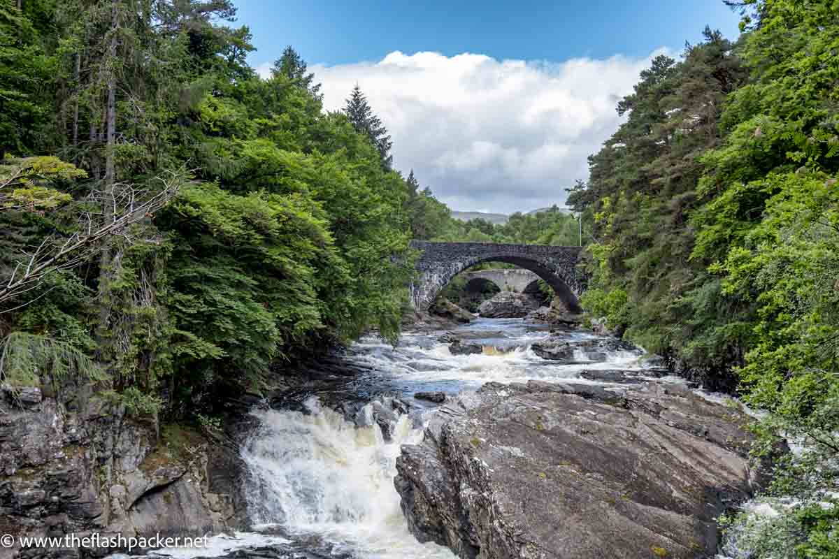 water cascading over rocks down a fast flowing river with stone bridge in background at ivermoriston scotland