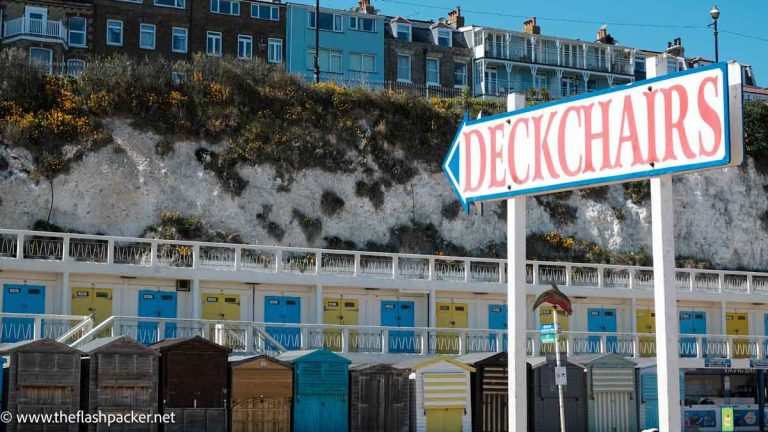 big sign saying deckchairs pointing to a row of beach huts