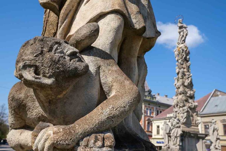 gnarled gothic stone sculpture of a devil under the foot of an angel