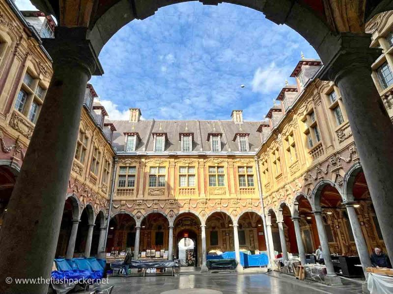 courtyard enclosed by colonnaded orange and red baroque buildings viewed through an arch