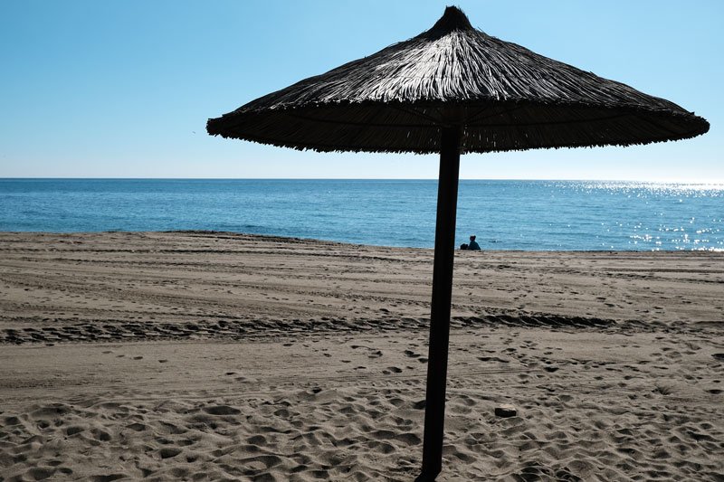 person settin by shoreline on sandy beach with huge umbrella in foreground