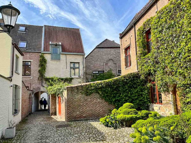 2 people walking through a narrow archway leading to a cobblestone yard