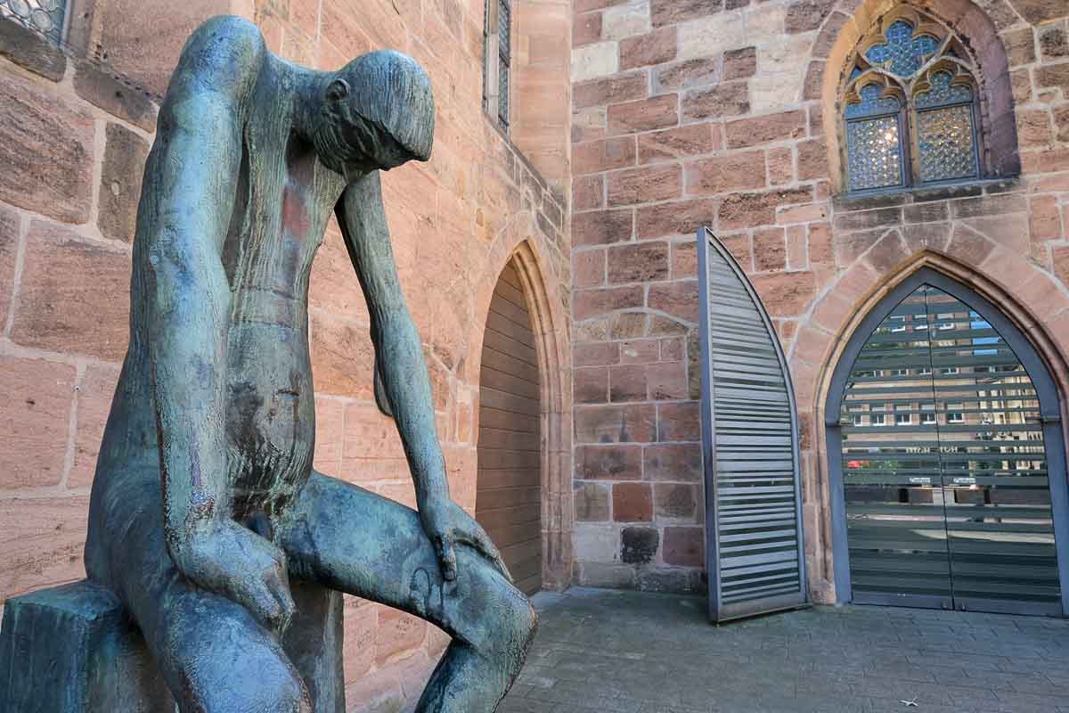 modern sculpture of a sitting man outside a church in nuremberg germany