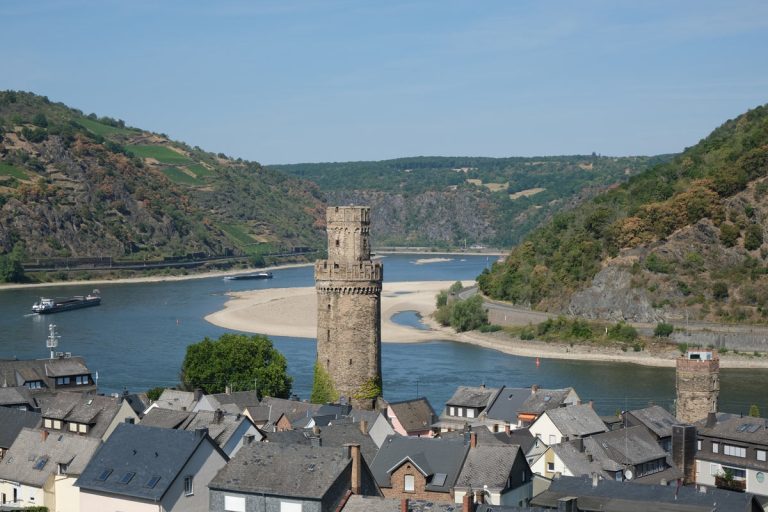 2 tall towers and the grey rootfops of the town of oberwesel germany against the background of a bend in the river rhine