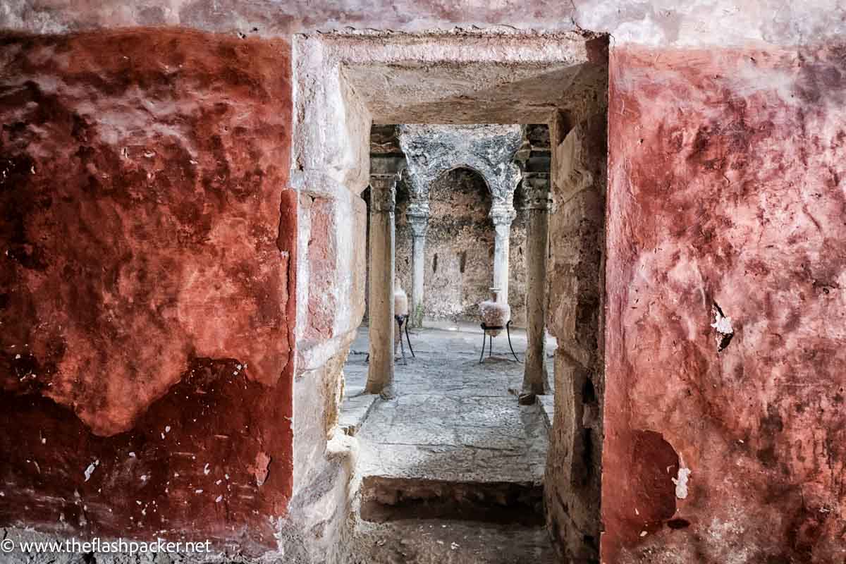 weathered red stone wall looking into old bath house with urns