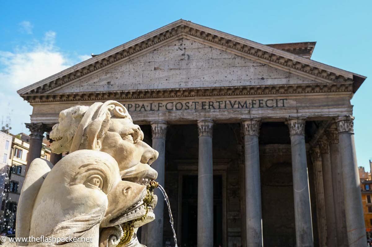 close up of fountain spouting water in front of collonaded facade of the pantheon in rome italy