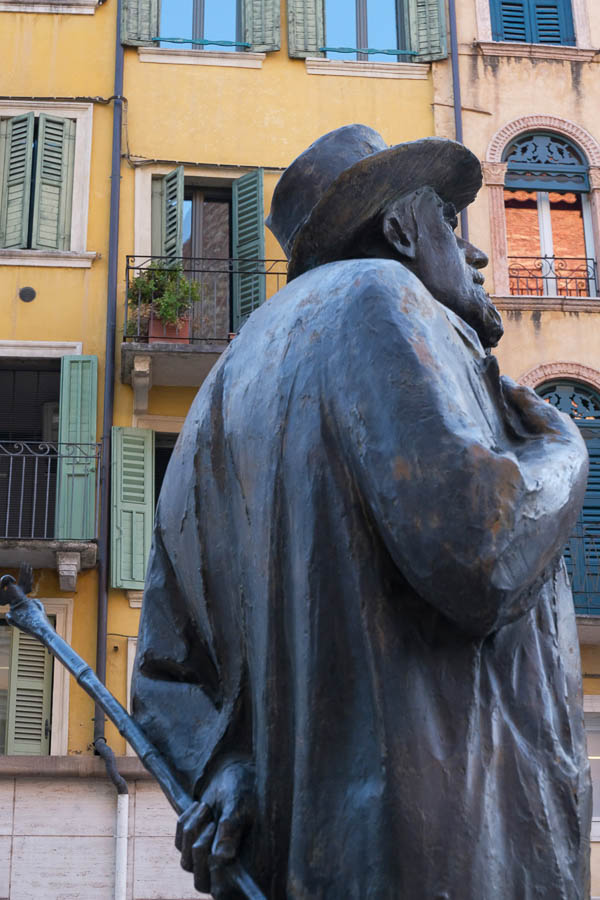 bronze statue of a man in front of pastel-coloured medieval buildings