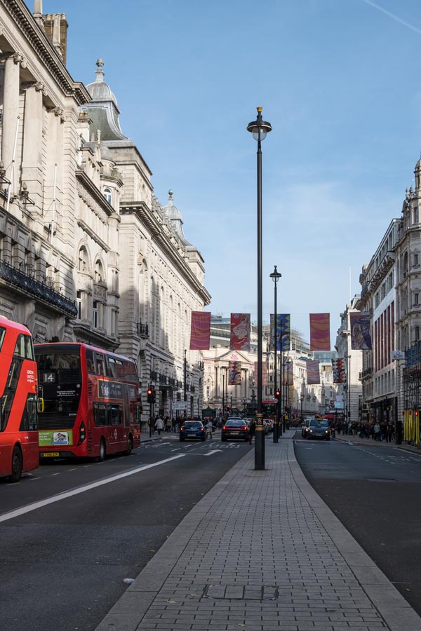 vehicles including red buses on a wide street in london