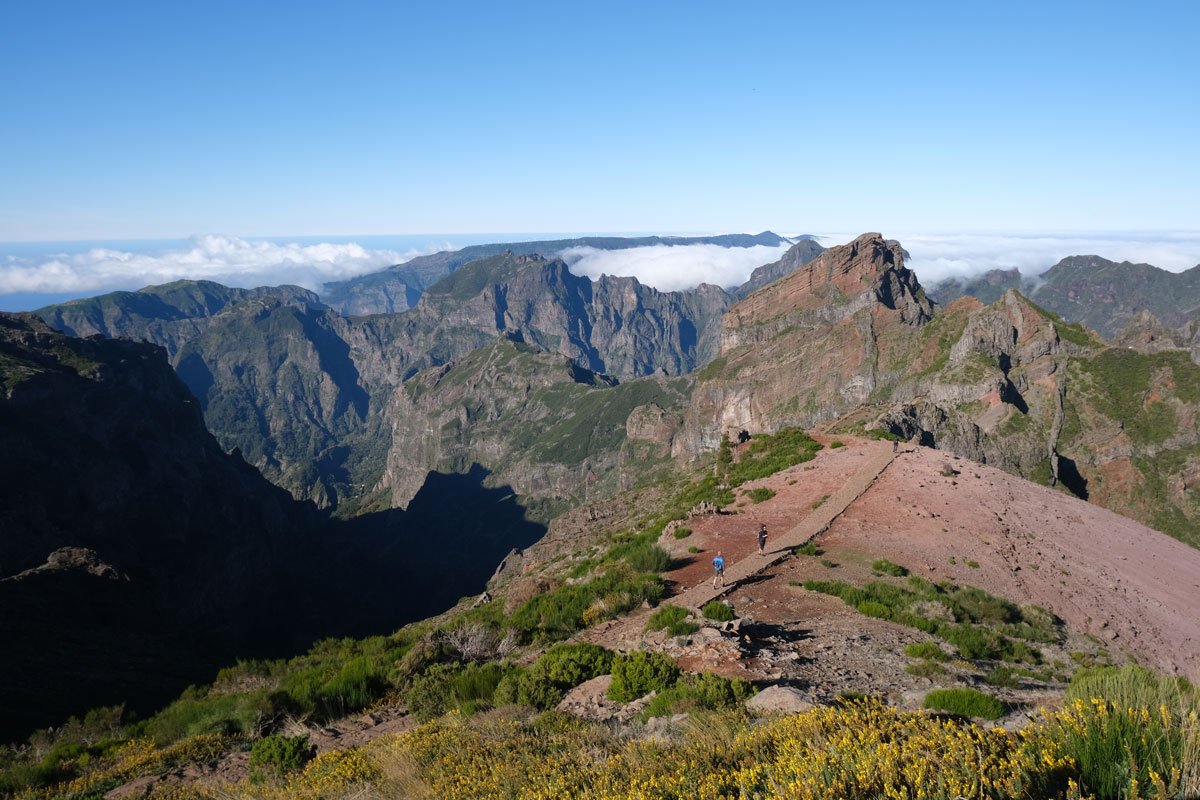 a few people waling across a path at the top of a mountain plateau