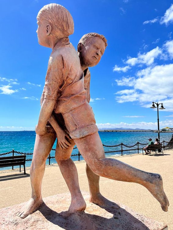 sculpture of 2 men wrestling on the seafront promenade under blue sky