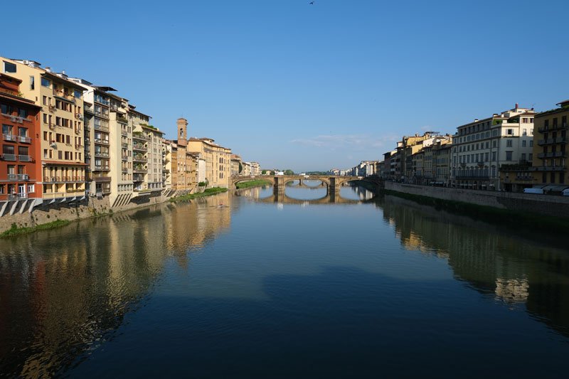 view of the river arno from Ponte Vecchio with buildings and bridge reflected in still river arno