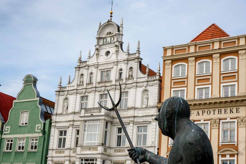 bronze statue of man with pitchfork in front of half-gabled houses