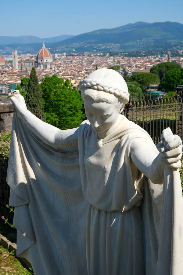 statue of angel with arms held out wide in front of a view of florence italy