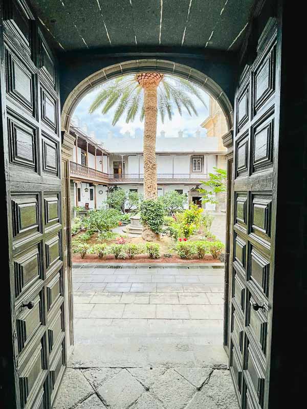 wooden doors opening onto a pretty cloister with a central palm tree