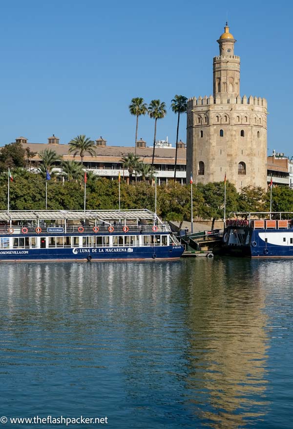 12 sided old tower reflected in river alongside river boat