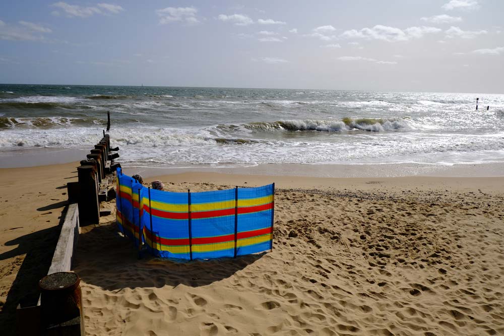 sunbathers sitting behind windbreak on southwold beach