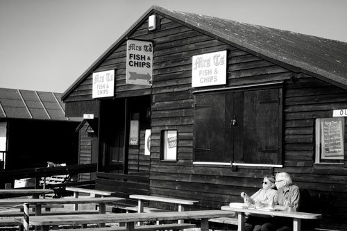 man and woman sitting at table outside wooden fish and chip shop