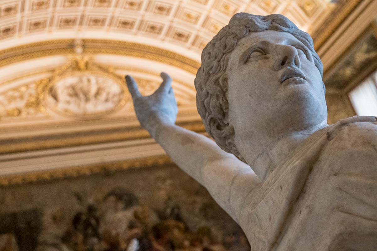 sculpture of a young man pointing his finger towards an ornate ceiling