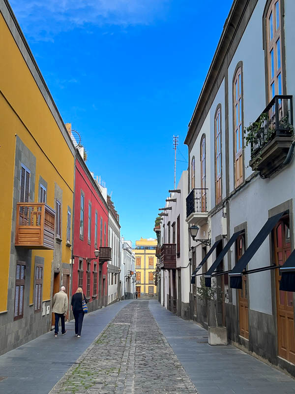 two people walking along a street lined with colonial buildings with wooden balconies in las palmas old town