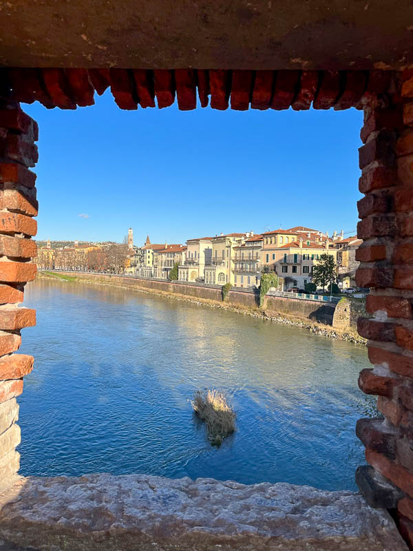 view of the riverbank of city of verona through opening in bridge