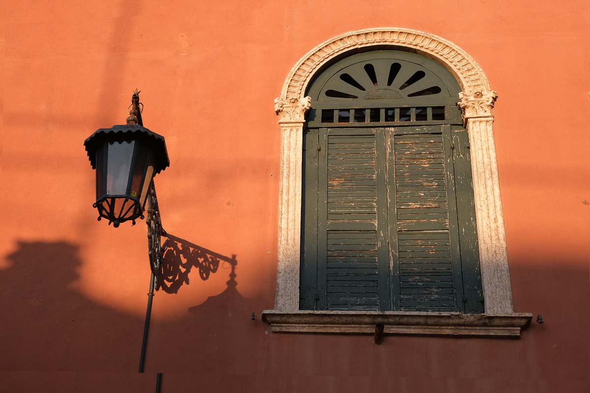 green shuttered window set in deep ochre painted wall with lampost