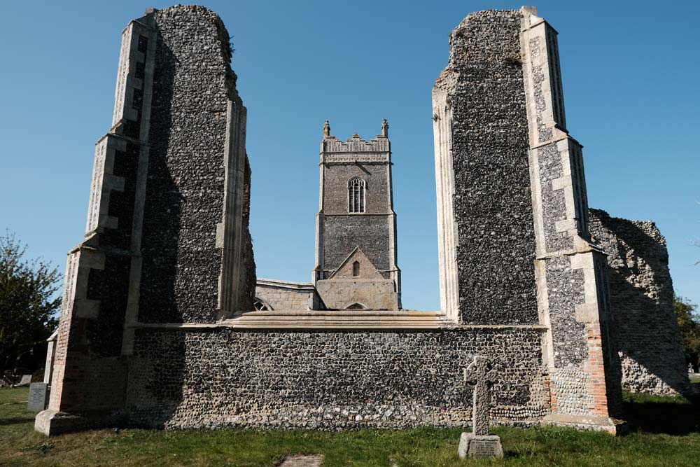 ruions of old church with newer church tower in background