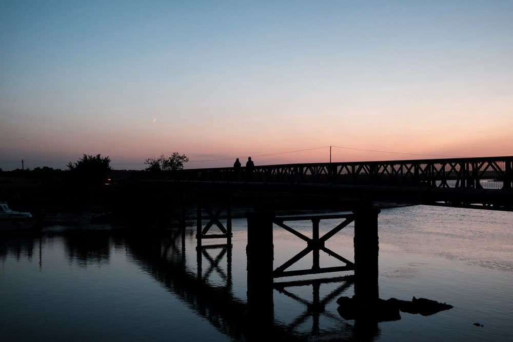 two people walking over a bridge at sunset