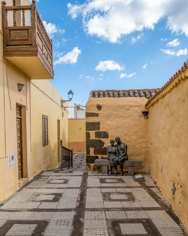 narrow street in old colonial town with bronze sculptures of 2 lovers on a bench